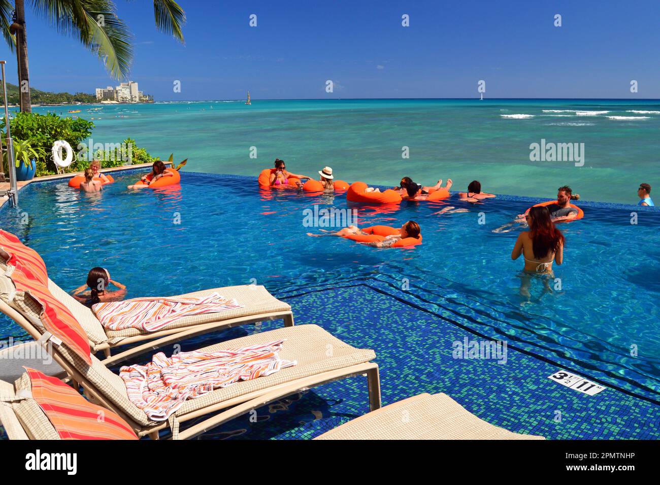 Hotel guests and vacation goers enjoy swimming in an infinity pool on a shore front resort on Waikiki Beach, Hawaii Stock Photo