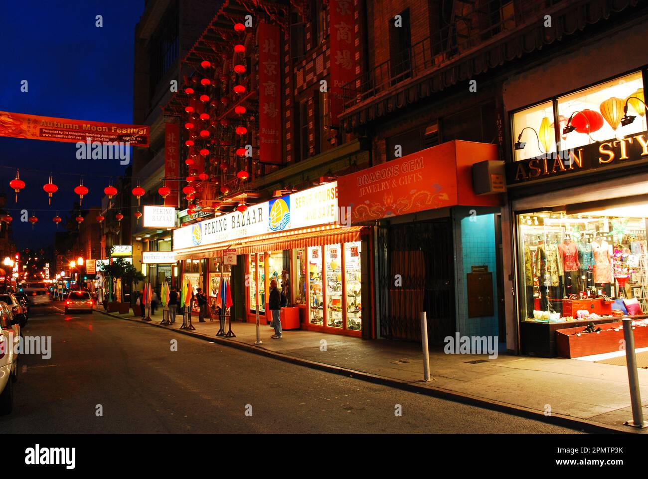 Chinese lanterns are strung across a street and illuminated at night in front of the stores in the Chinatown district in San Francisco Stock Photo