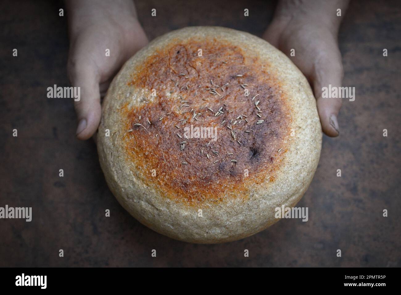 Homemade crusty loave of bread on wooden background. Baker holding fresh bread in the hands. Still life concept. Dark mood.view from above Stock Photo