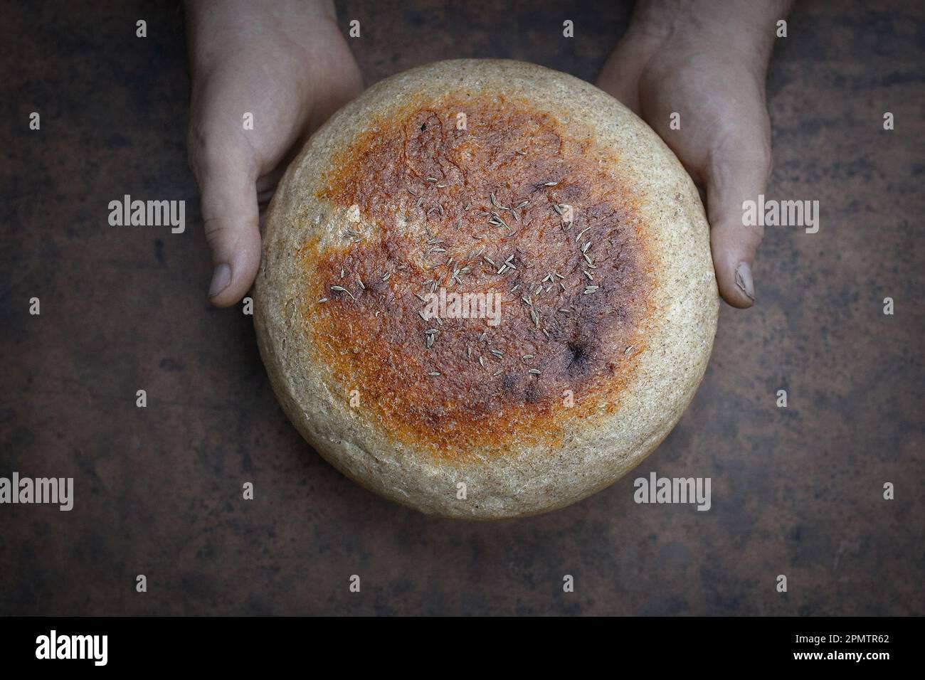 Homemade crusty loave of bread on wooden background. Baker holding fresh bread in the hands. Still life concept. Dark mood.view from above Stock Photo