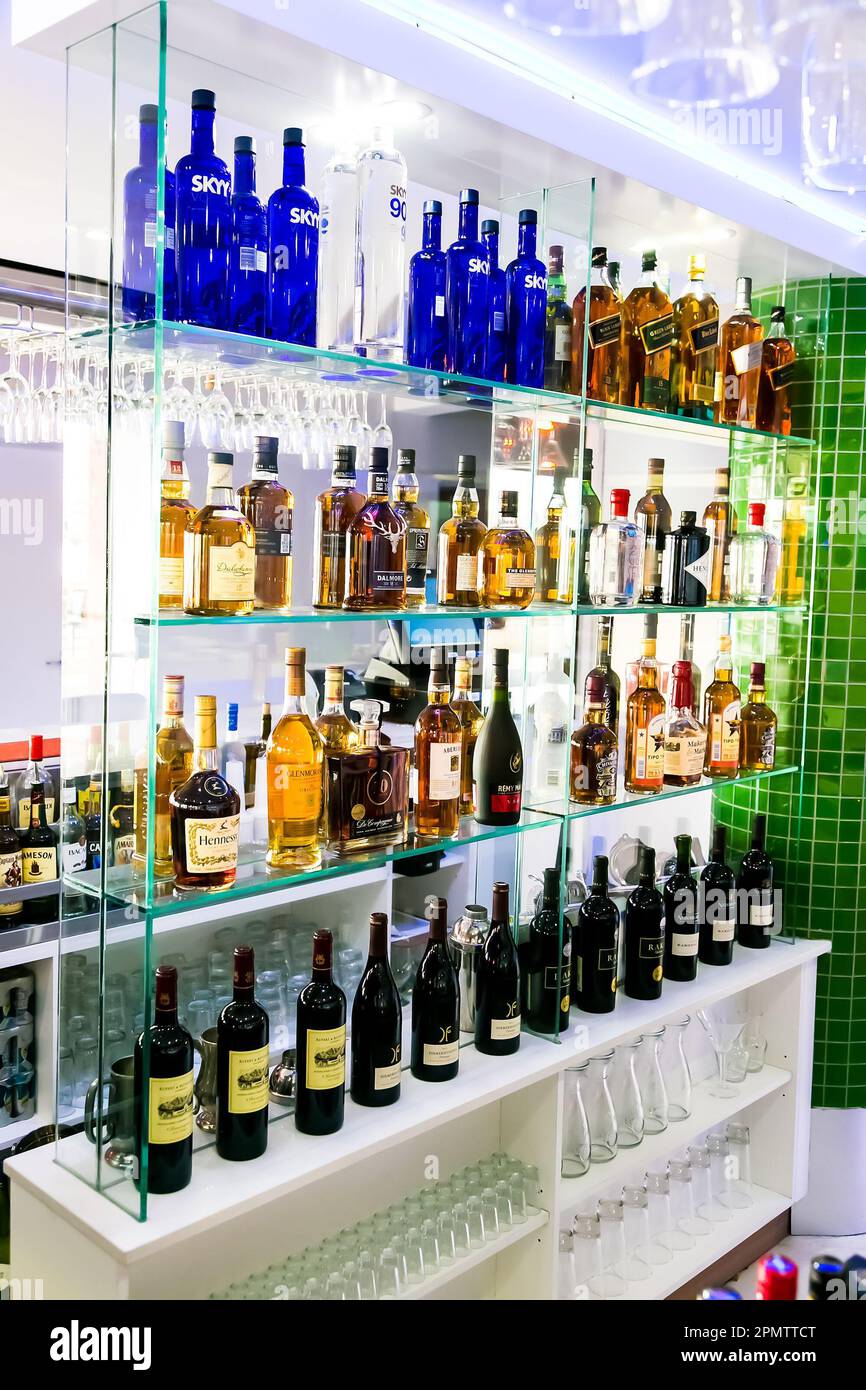 A well-stocked bar with a variety of liquor bottles arranged on shelves, accompanied by wine glasses and other glasses for serving Stock Photo