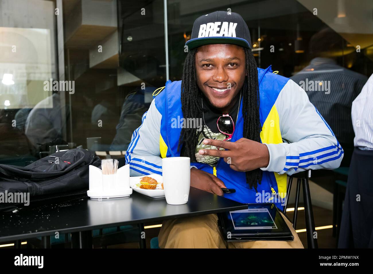 A young man in a bright blue and yellow jacket is seated at a table with a tablet Stock Photo