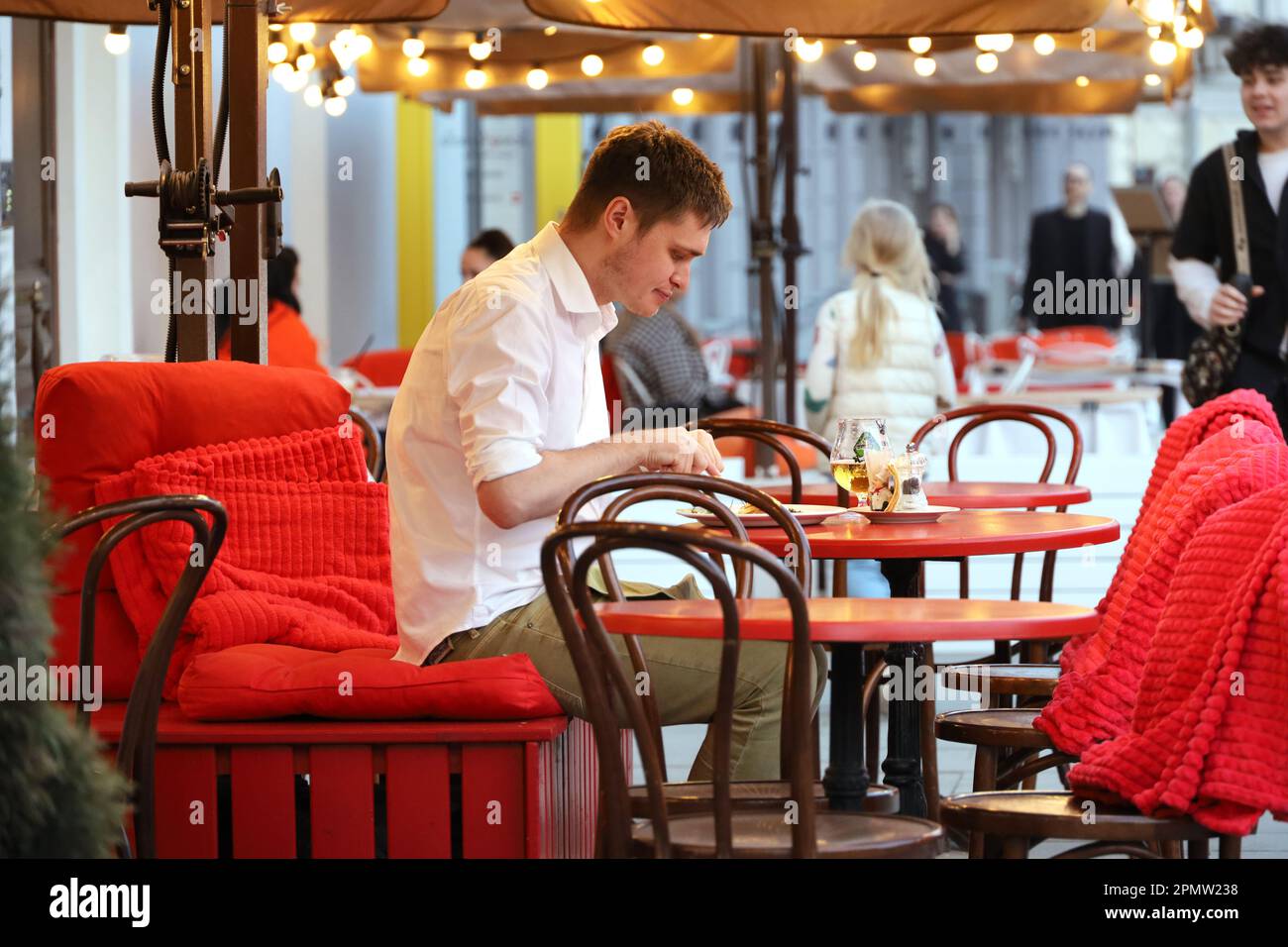 Young man eating dinner on the spring terrace of street cafe on people