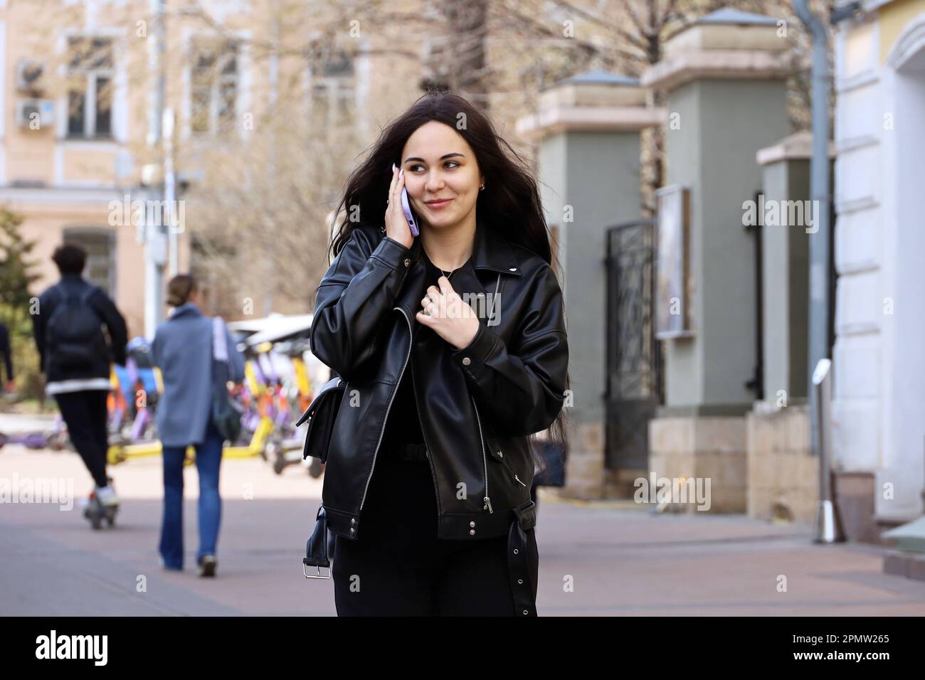 Attractive smiling girl talking on smartphone while walking down street. Using mobile phone in spring city Stock Photo