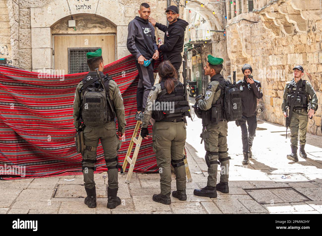 Israeli soldiers confront men hanging a carpet on a wall at the Old City in Jerusalem Stock Photo