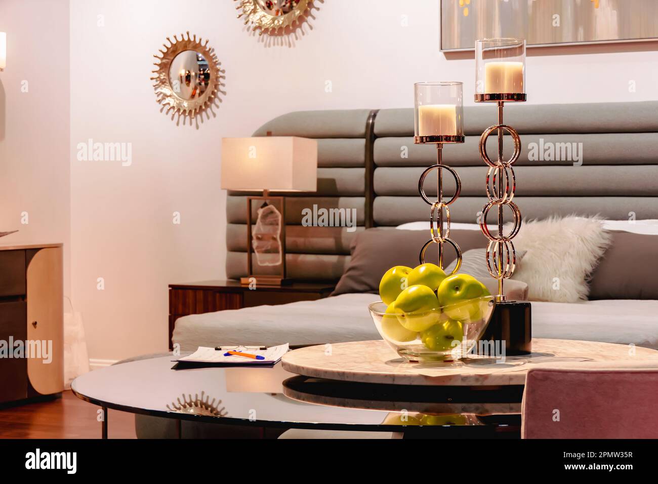 Two golden candlesticks and green apples in a glass vase stand on the