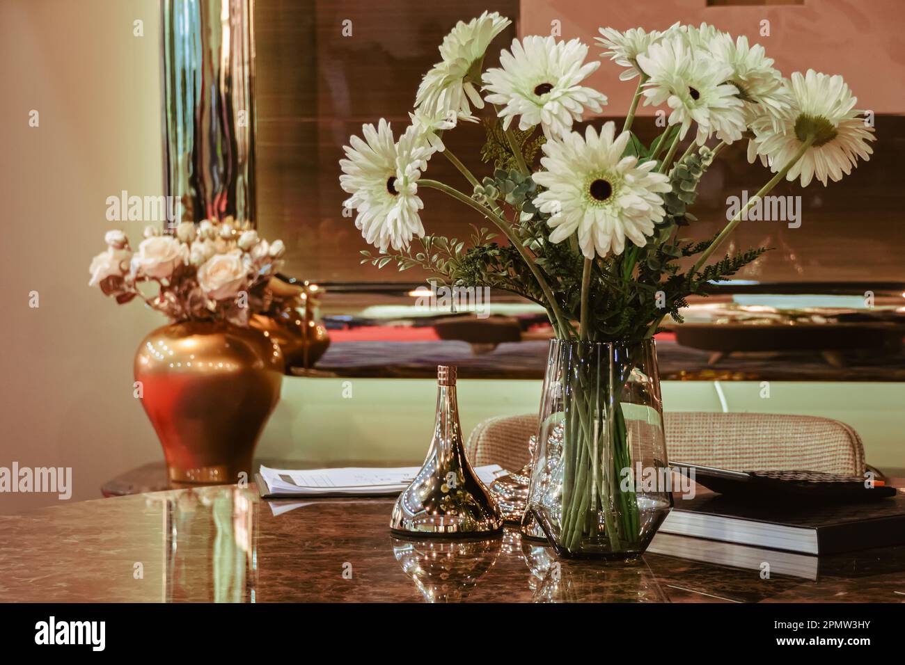 White gerberas in a vase near the mirror stand on the table. Stock Photo