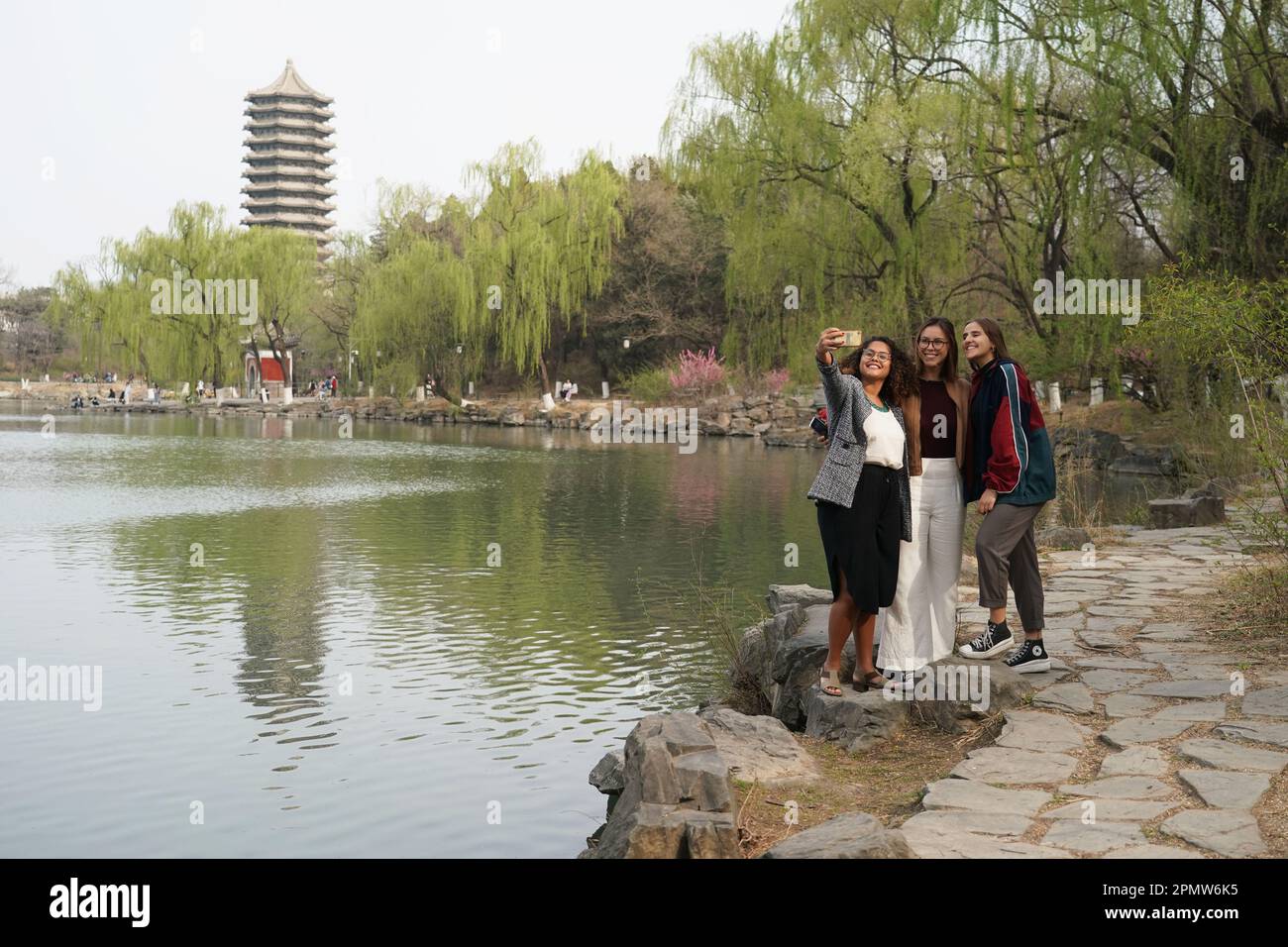 (230415) -- BEIJING, April 15, 2023 (Xinhua) -- Rafaela (L), Manuela (C) and Maria take a selfie near the Weiming Lake of Peking University in Beijing, capital of China, March 31, 2023. Maria Eduarda Variani, Rafaela Viana dos Santos, Manuela Boiteux Pestana, and Marco Andre Rocha Germano are Brazilian students studying in the Master of China Studies program at the Yenching Academy of Peking University in China. The four of them have been interested in Chinese culture since they were young. After arriving in Beijing, they have been impressed by the Chinese capital's profound cultural herit Stock Photo