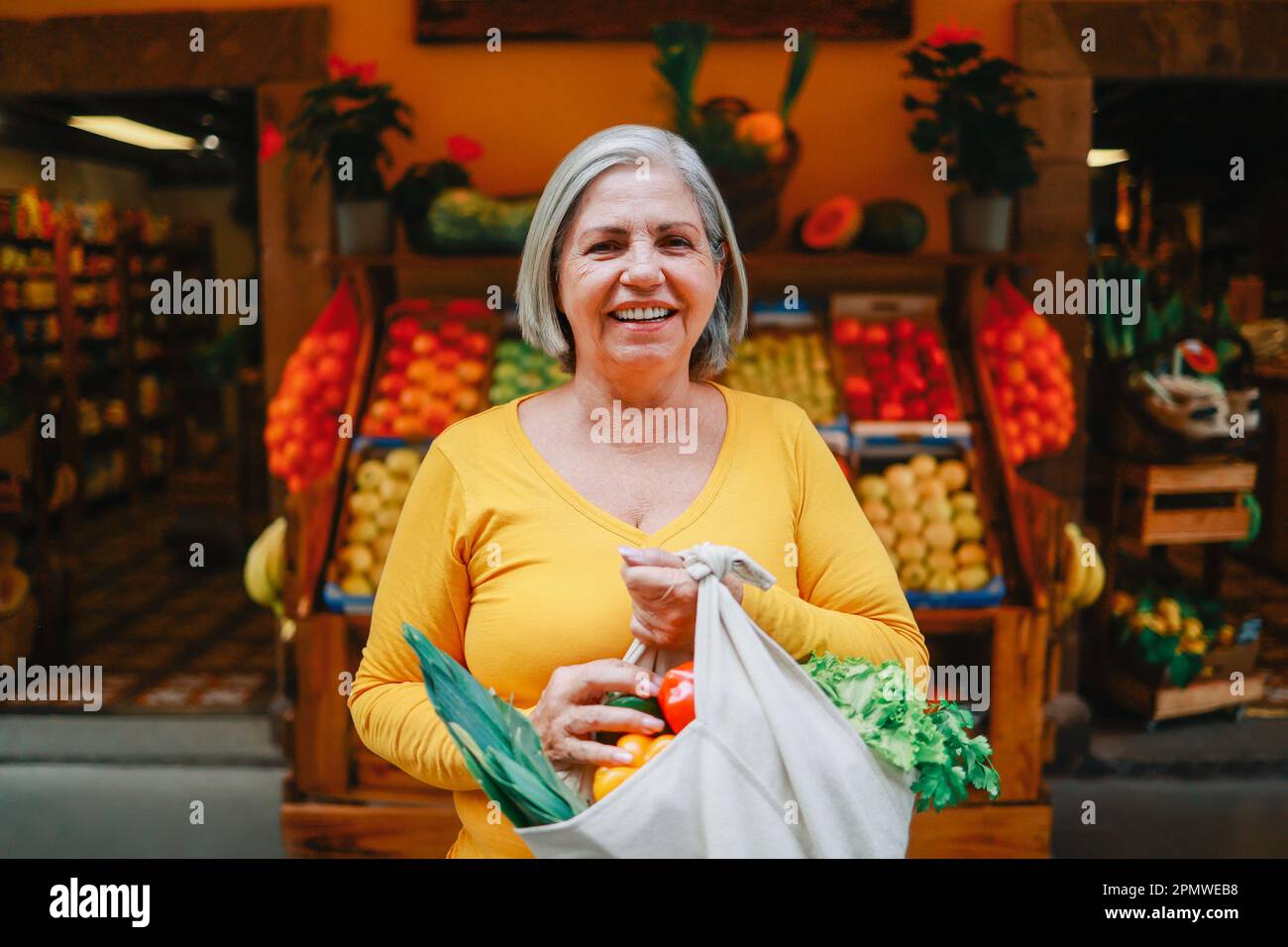 Zero waste food retail - Happy senior woman holding reusable bag of fresh vegetables at local market store - Sustainable eco concept - Focus on face Stock Photo