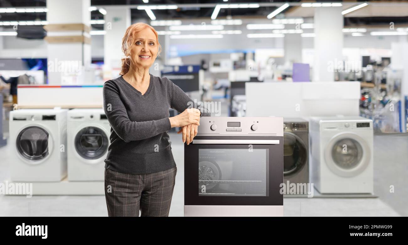 Happy mature woman posing inside a store and leaning on an oven Stock Photo