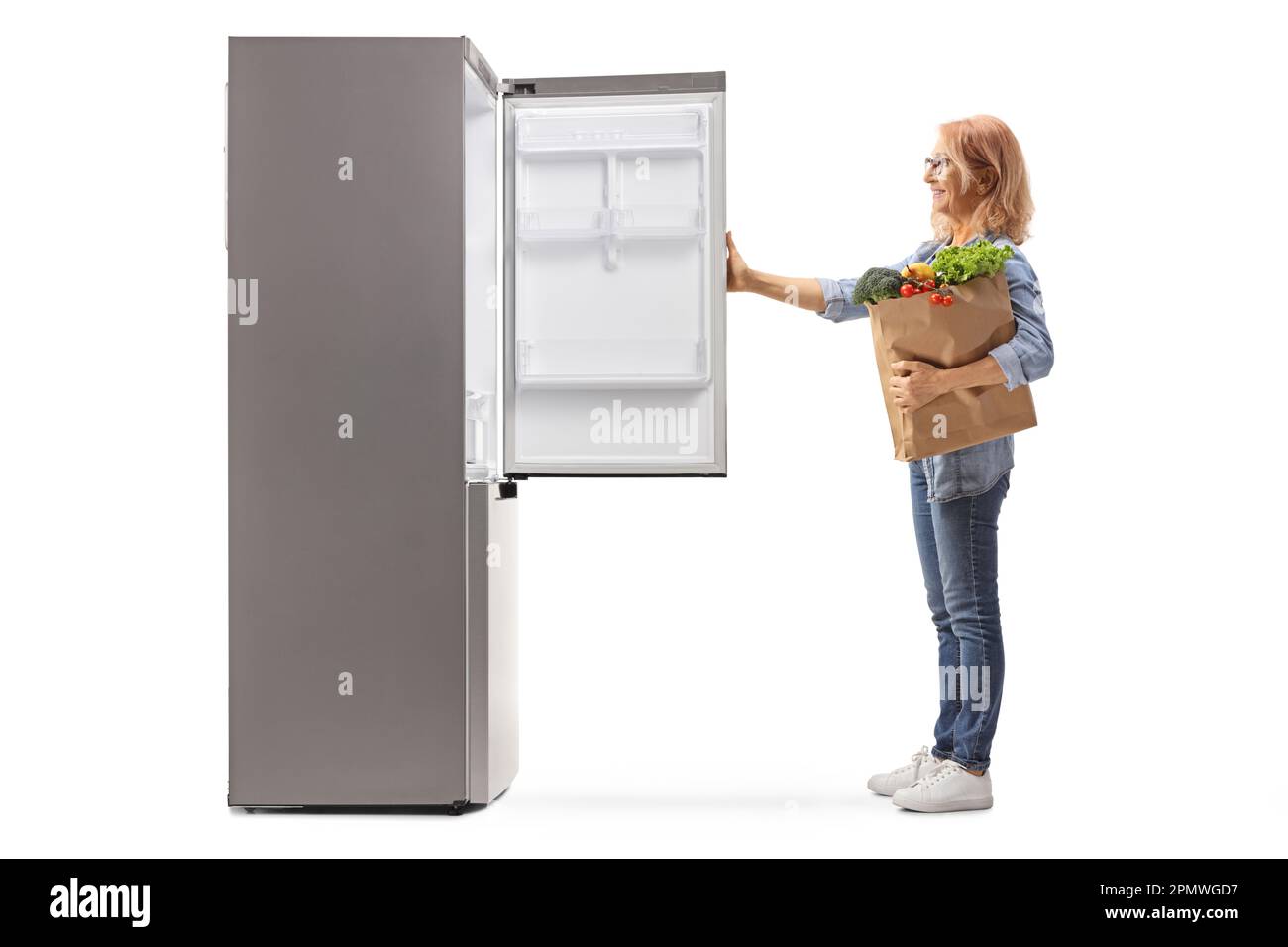 Woman with a grocery bag looking at an empty fridge isolated on white