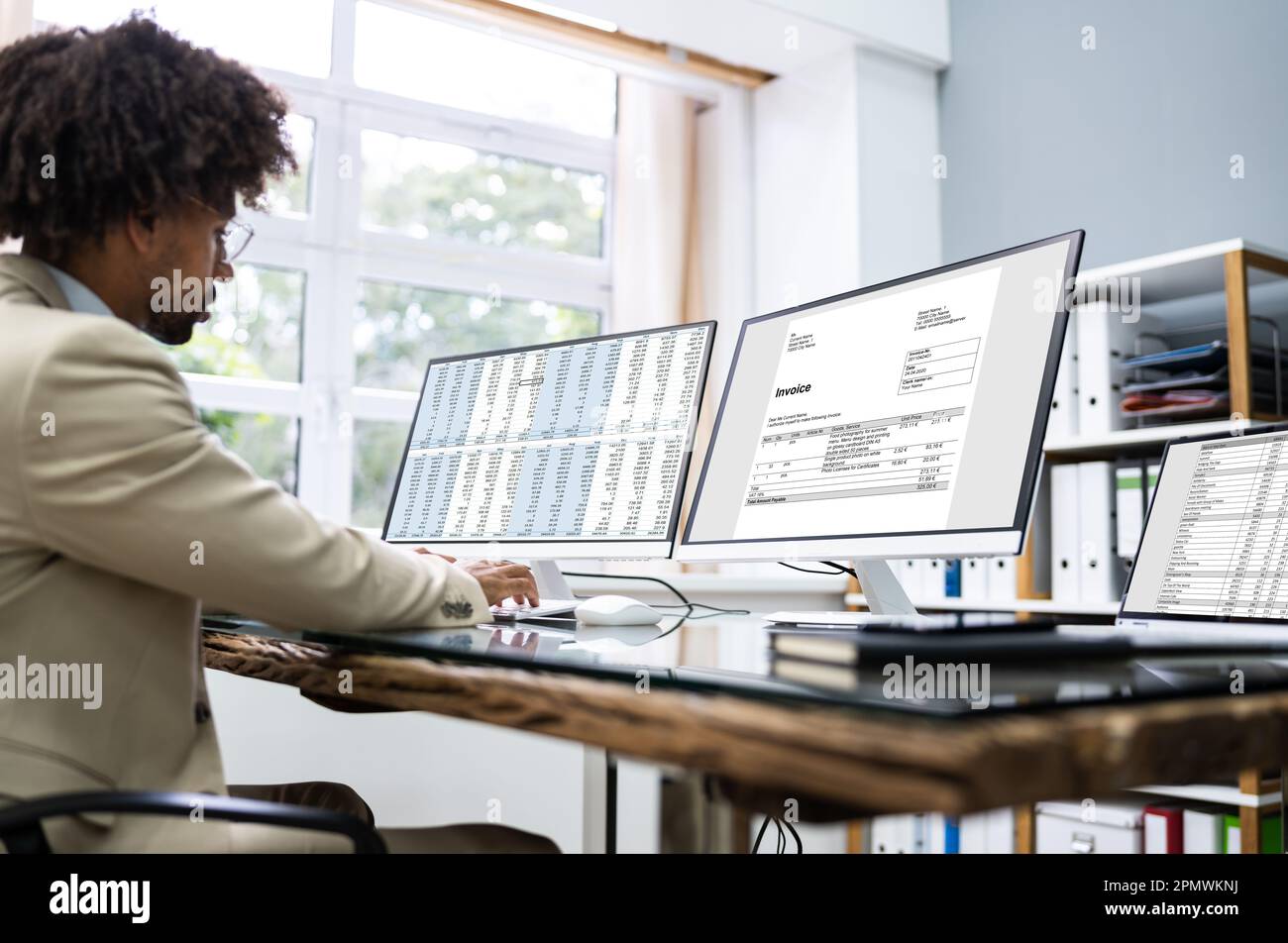 Looking At Invoice And Spreadsheet On Computer At Work Stock Photo