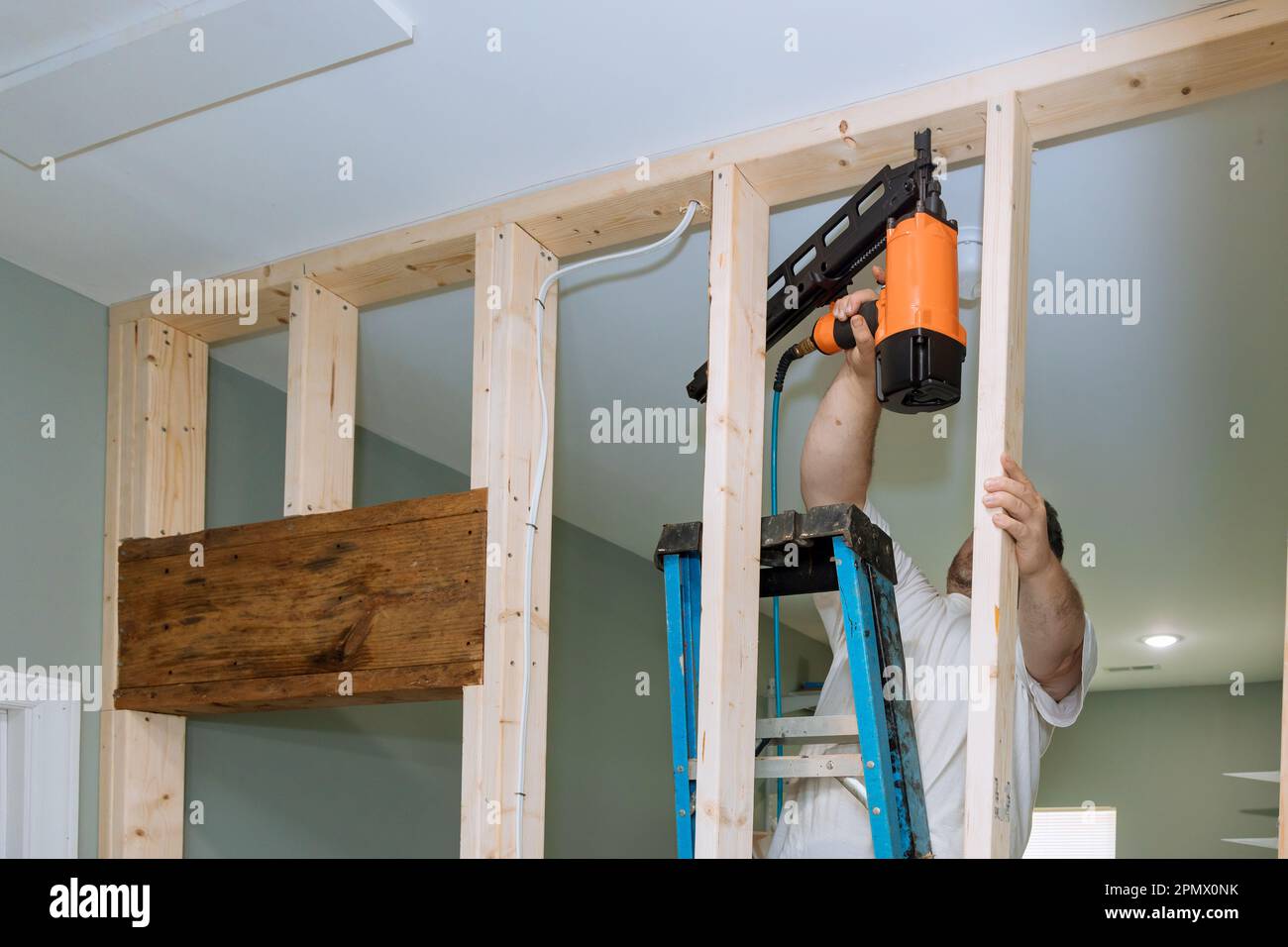 With help of an air hammer, builder nails wooden beams to frames house ...