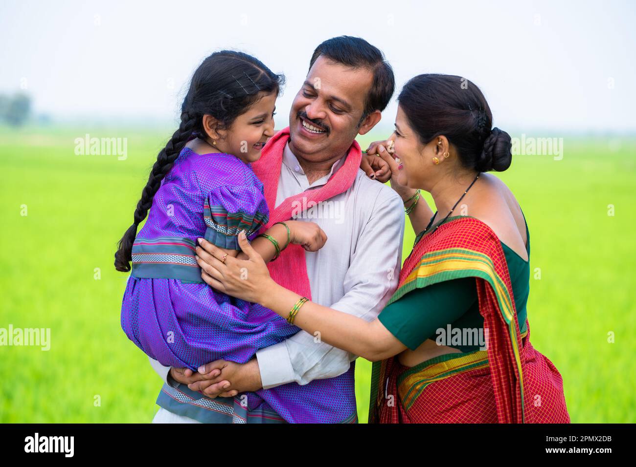 Happy mother playing with daughter by cuddling while father holding her at village farmland - concept of family bonding, parenthood and togetherness. Stock Photo