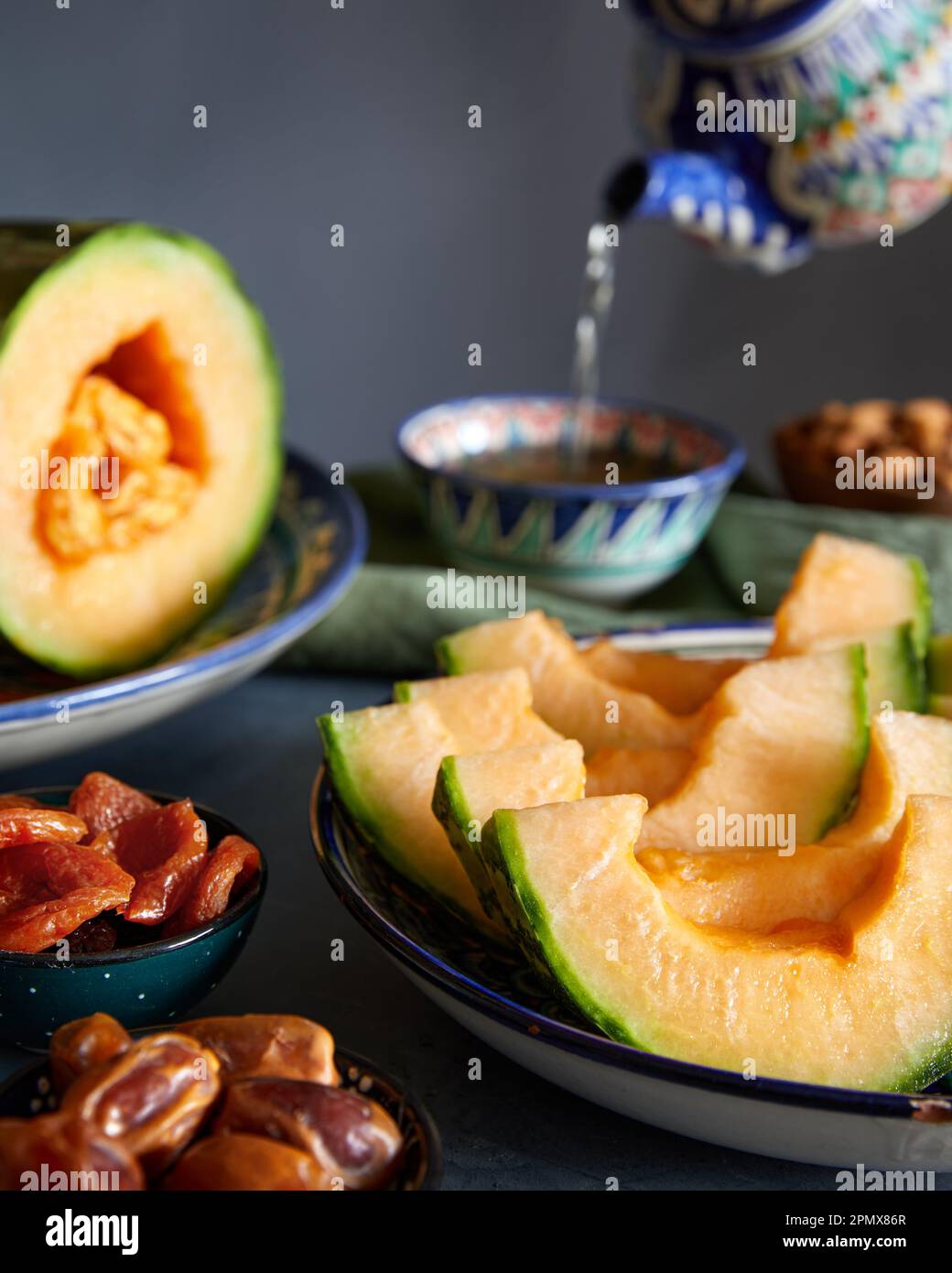 Traditional Uzbek oriental cuisine table with yellow melon date, dry apricot and pot of tea at