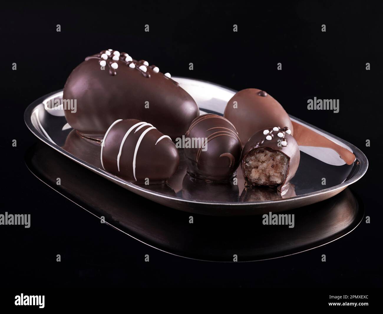 Silver serving platter with noble decorated marzipan chocolates on black background with reflections. Stock Photo