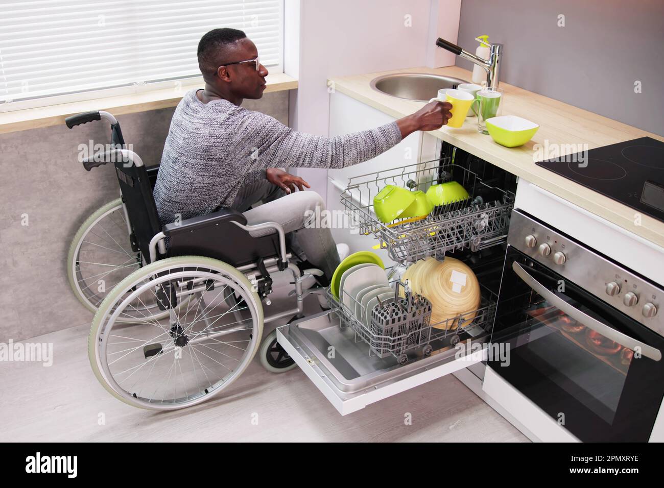 Young Man Sitting On Wheelchair Arranging Plates In Dishwasher Stock Photo