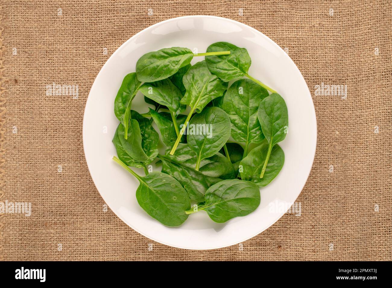 Fresh green spinach leaves in plate on jute cloth, macro, top view