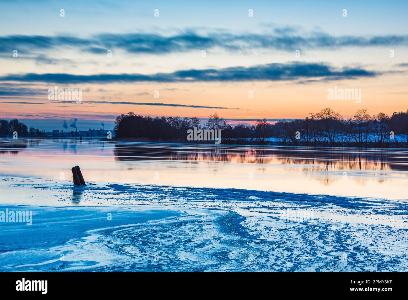 The beauty of nature is reflected in the frozen river at dusk on a cold winter night. The sky and shore glisten with ice as the sun sets. Stock Photo