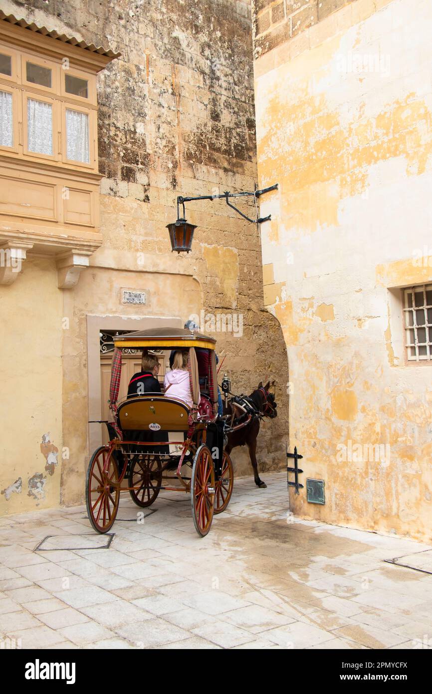 Mdina, Malta - November 13, 2022: Tourists riding in a traditional horse carriage for a sightseeing tour in rear view Stock Photo