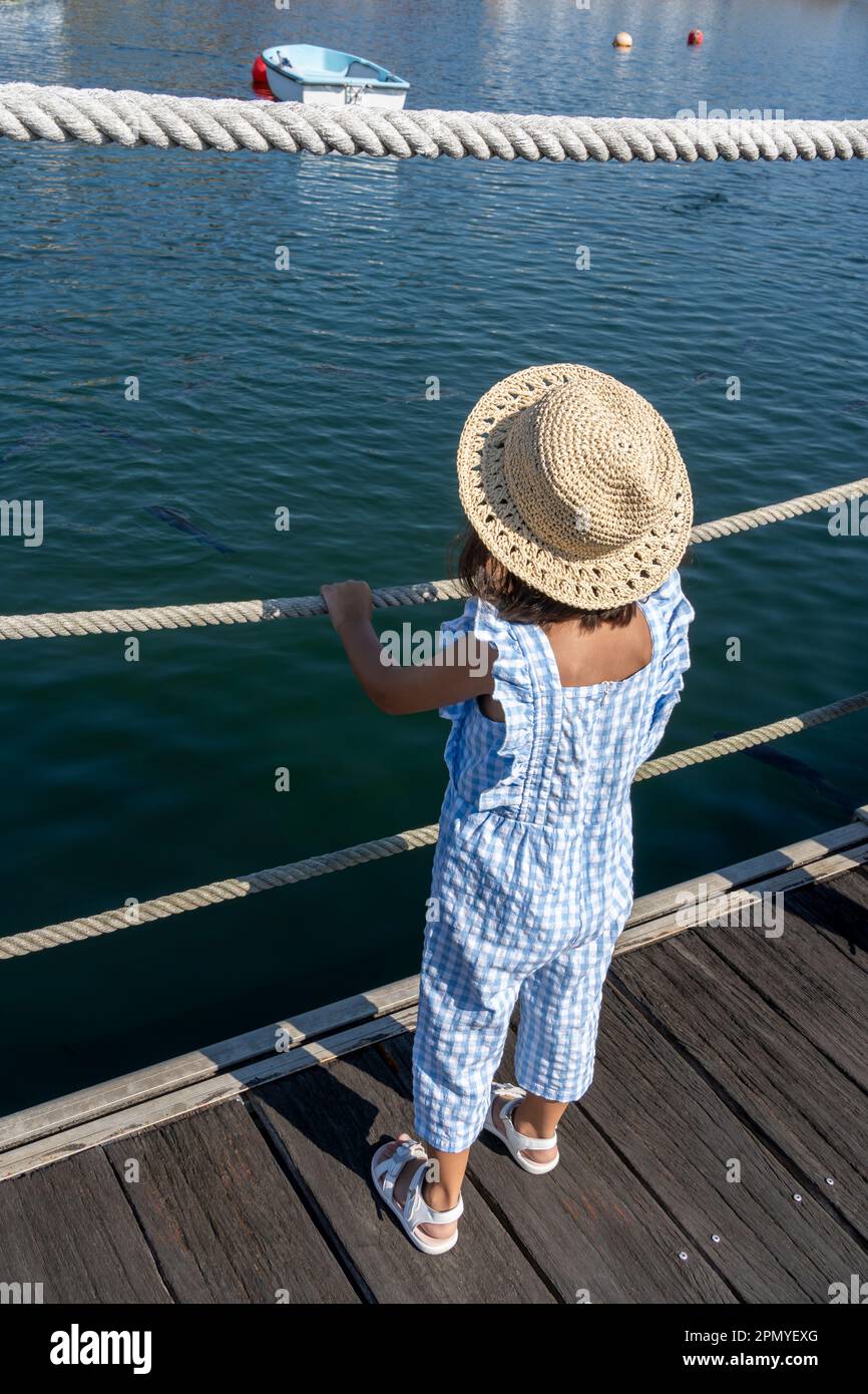 little girl in a straw hat in the harbour looking at the fish in the sea  Stock Photo - Alamy