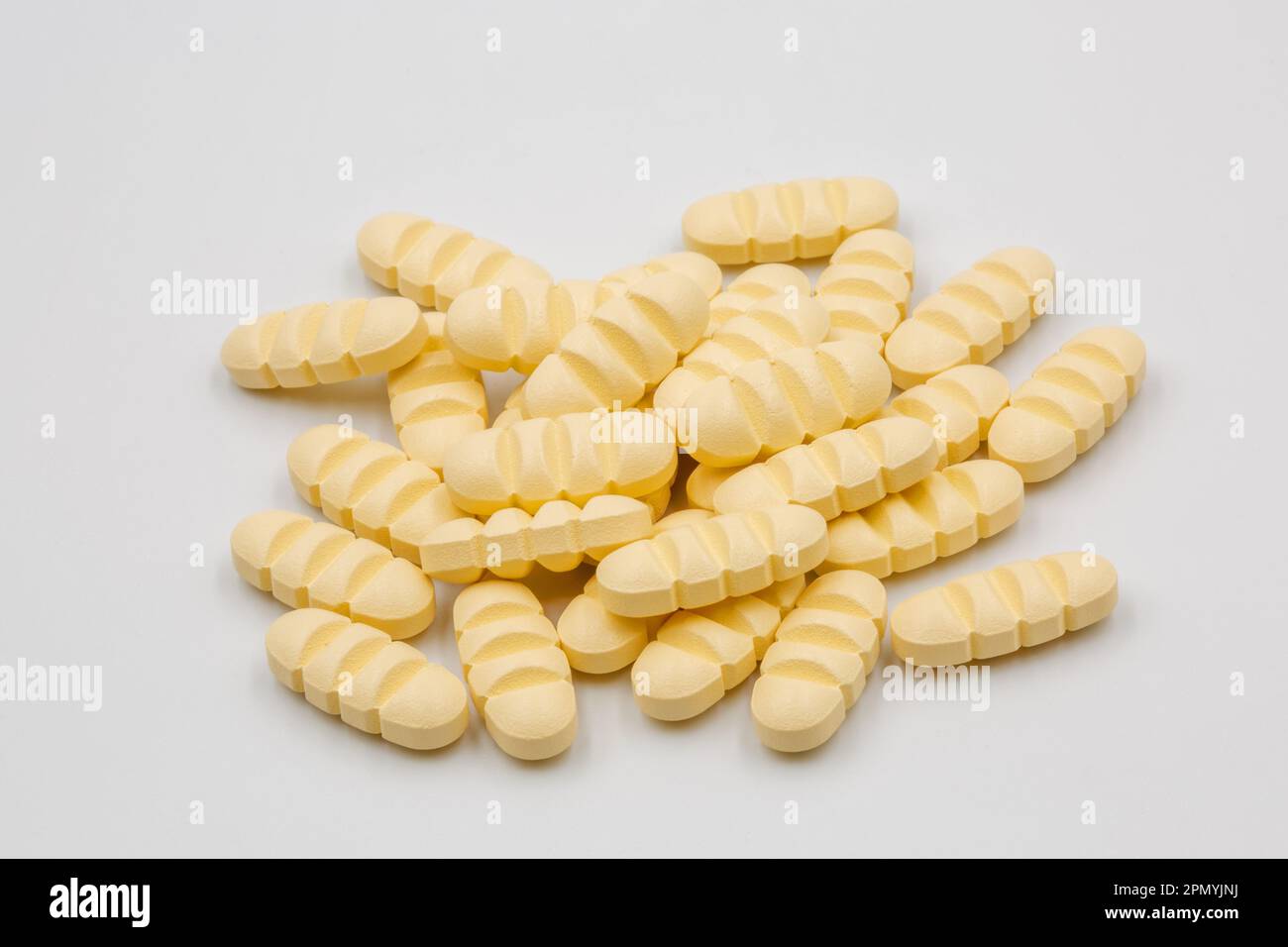 A pile of yellow oblong tablets with dividing strips for dividing into four parts closeup on white. Stock Photo