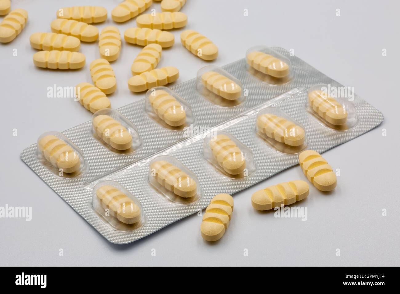 Blister with yellow oblong tablets with dividing strips for dividing into four parts closeup on white. Stock Photo