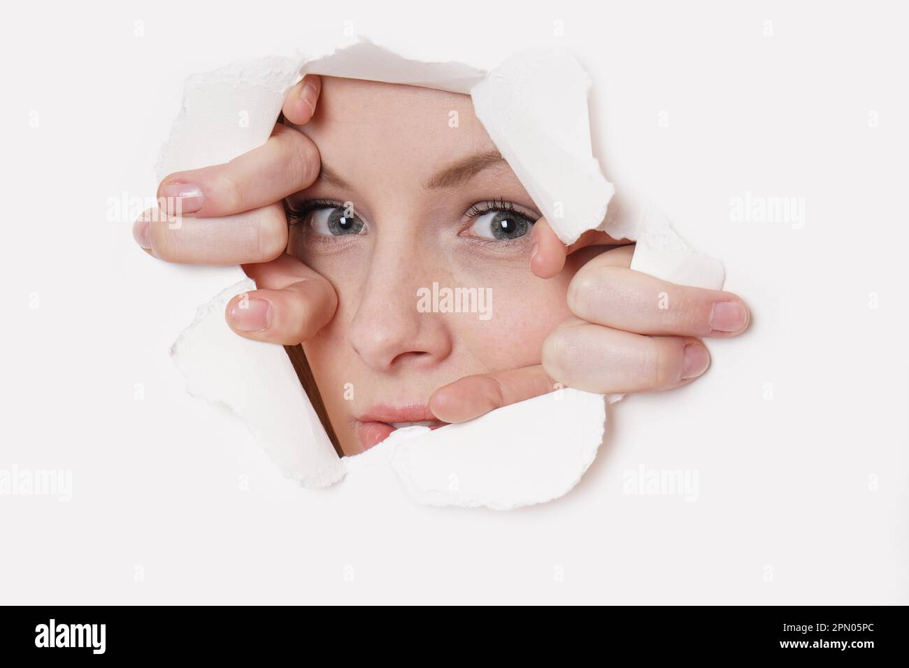 young woman peeking through hole in paper wall Stock Photo