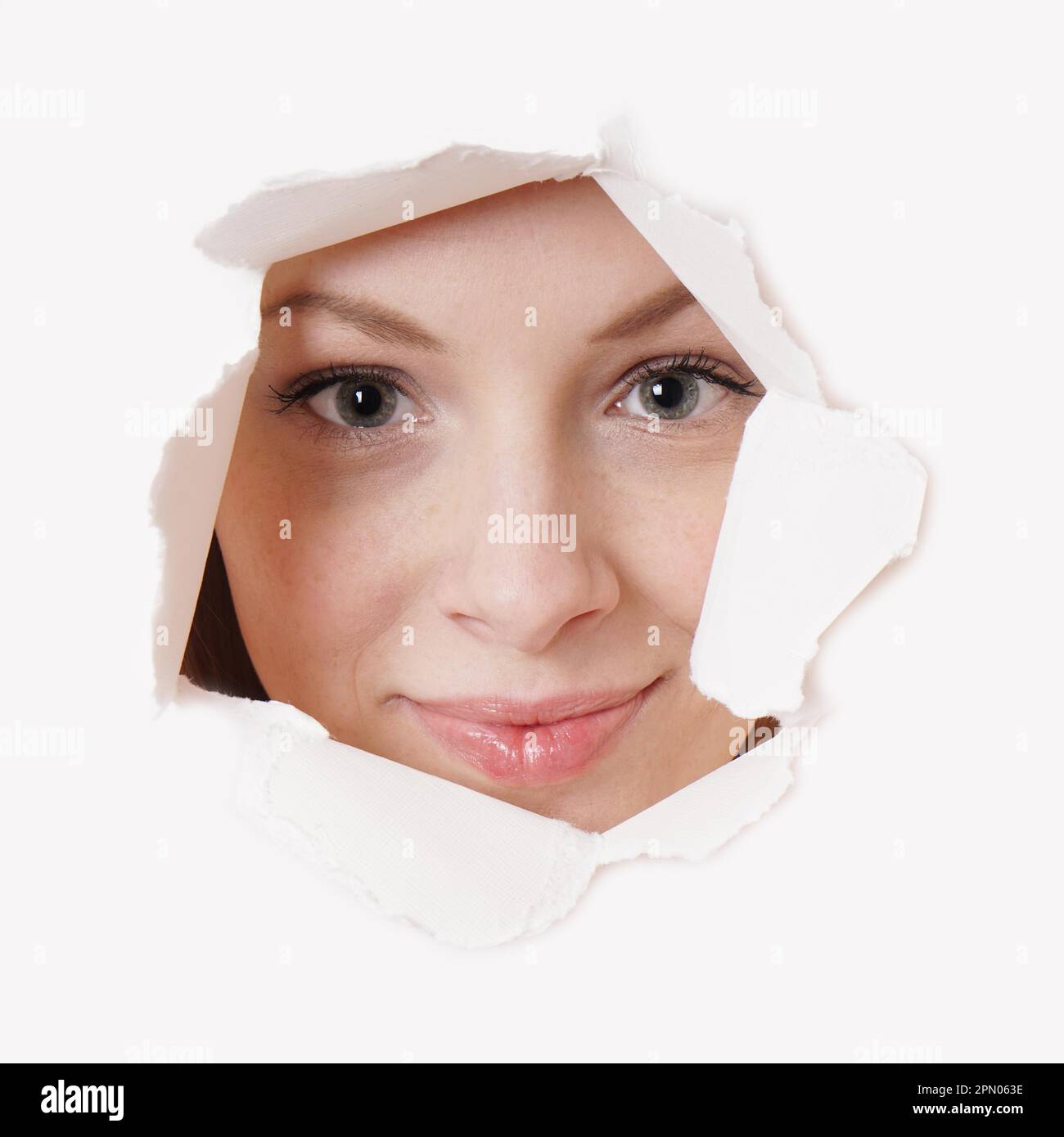 smiling young woman peeking through hole in paper wall Stock Photo