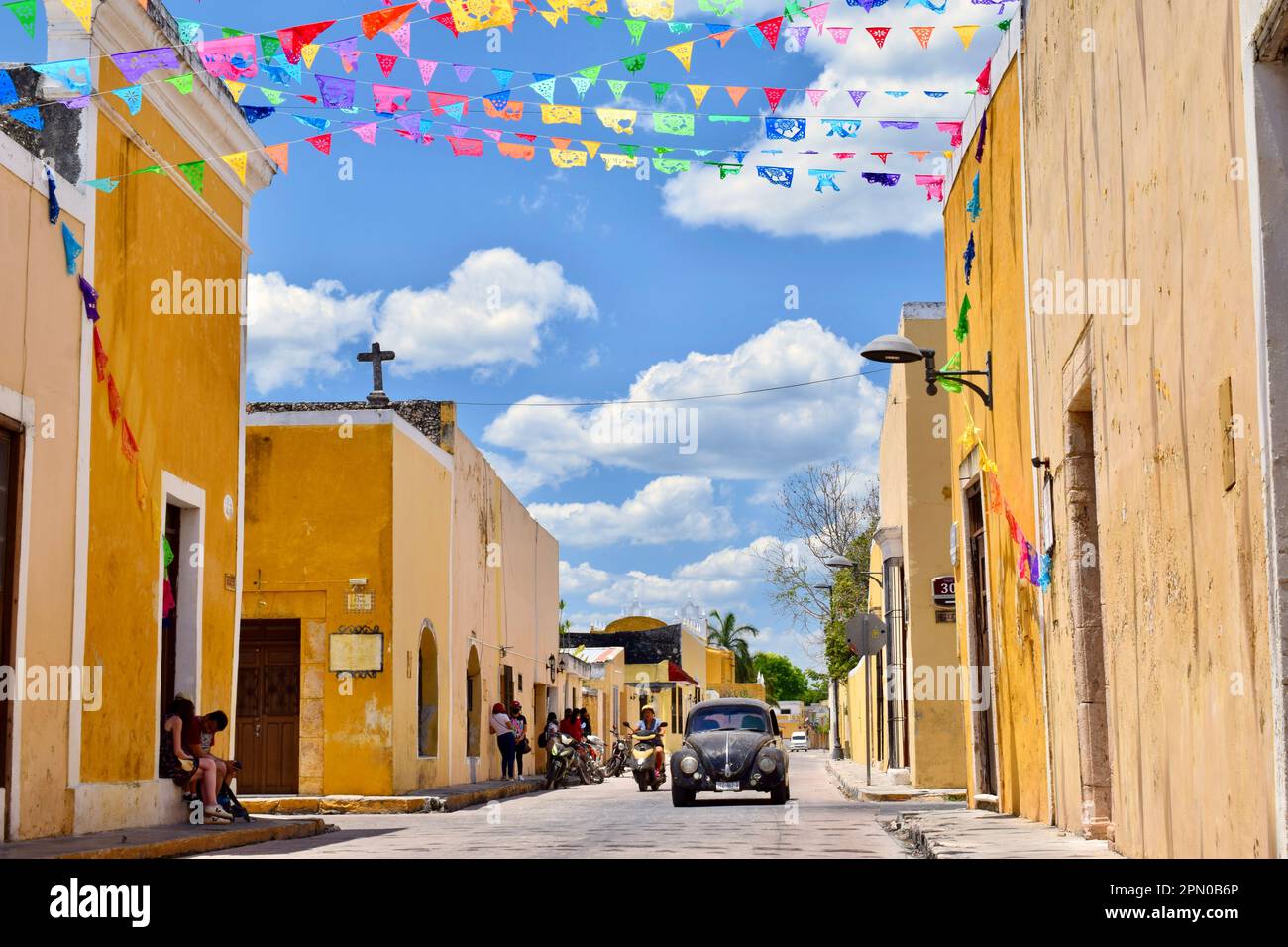 A street scene with people, a scooter, and a Volkswagen beetle in the picturesque town of Izamal, Yucatan, Mexico. Stock Photo