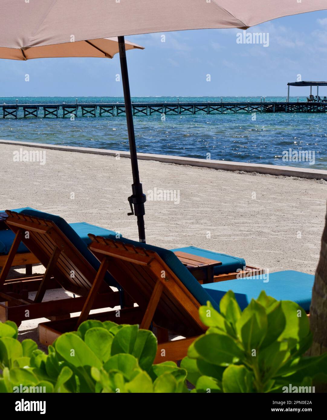 Lounge chairs under a parasol and facing the sea, at the beach, on a sunny day in San Pedro, Ambergris Caye, Belize, Caribbean/Central America. Stock Photo