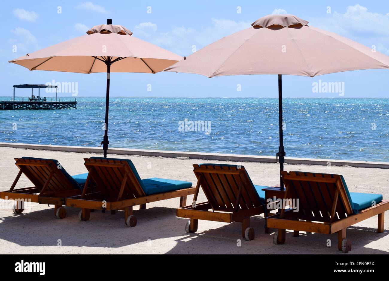 Lounge chairs at the beach under parasols and facing the sea on a sunny day in San Pedro, Ambergris Caye, Belize, Caribbean. Stock Photo