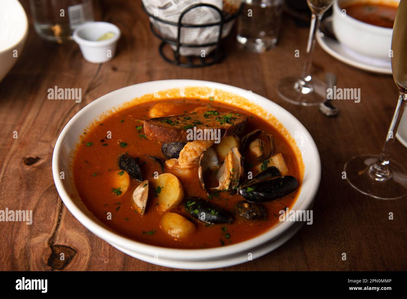 Steamed mussels in white plate with tomatoes, potatoes and bread, garnished with garlic in a restaurant setting Stock Photo