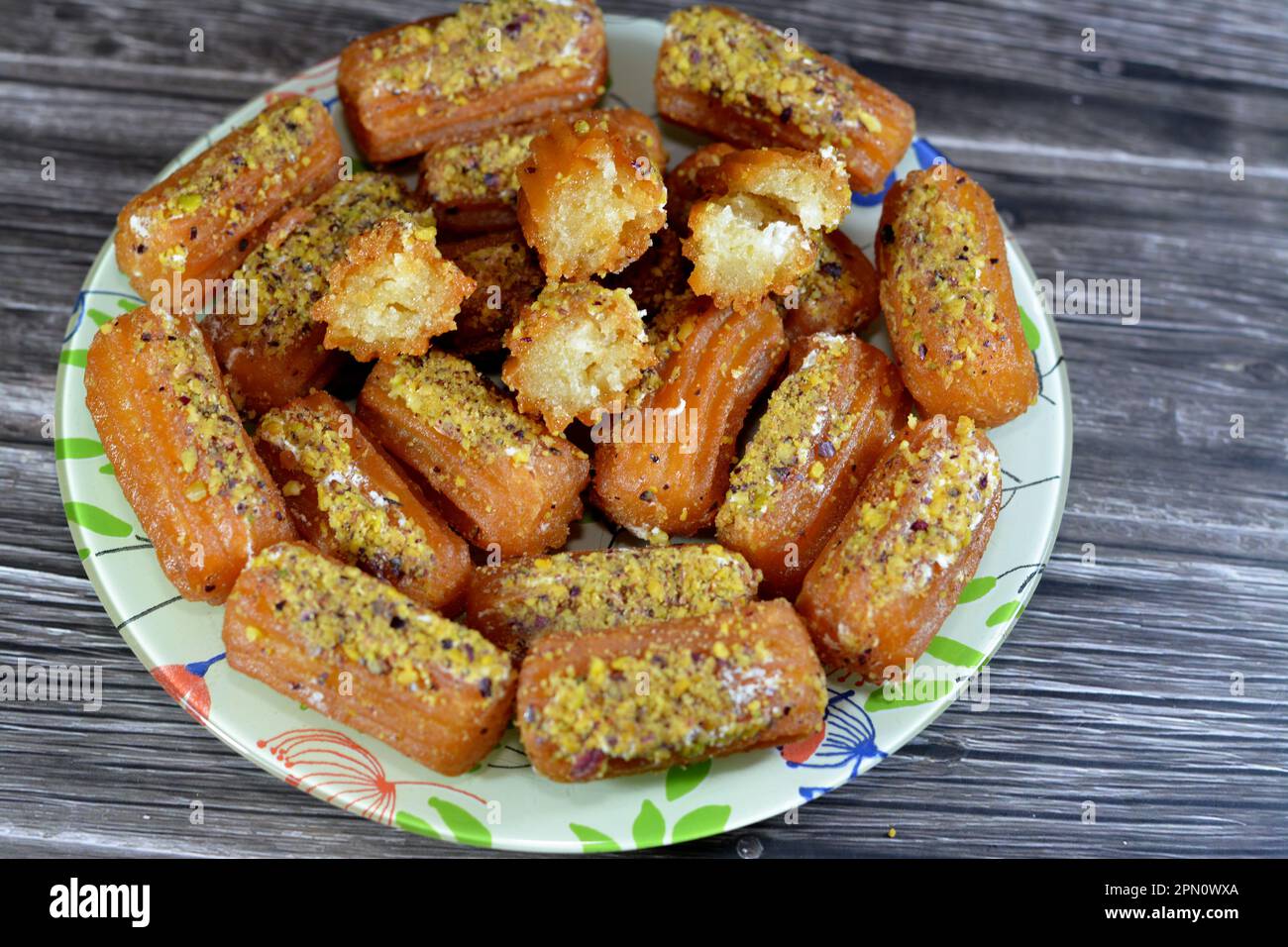 Tulumba, Bamiyeh or Balah El Sham stuffued with whipped cream and covered with pistachios and nuts, deep fried batter dessert soaked in syrup, similar Stock Photo