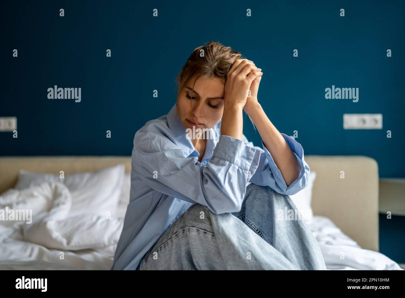 Young unhappy woman sitting on bed at home waking up depressed feeling sad and miserable Stock Photo