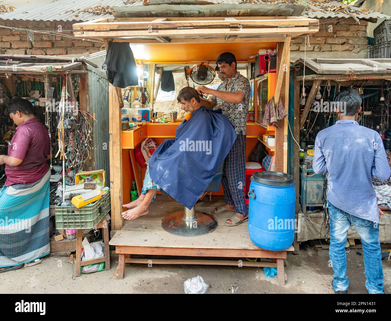 Man getting his hair cut at a tiny barbershop in Dhaka, the capital of Bangladesh. Stock Photo