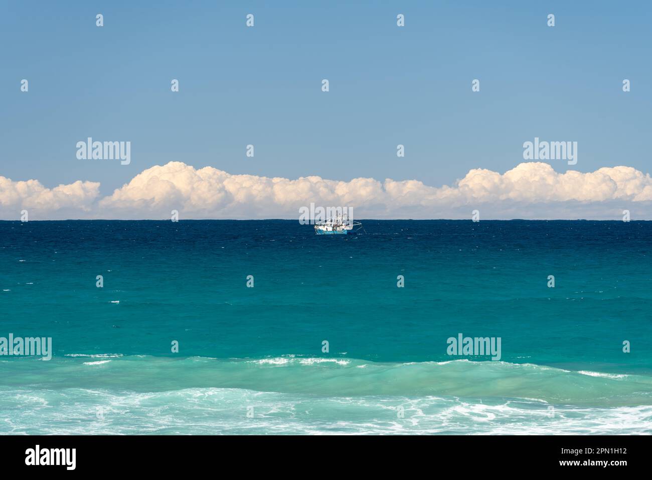 Single fishing trawler afloat on a turquoise sea, with a strip of cheer ...