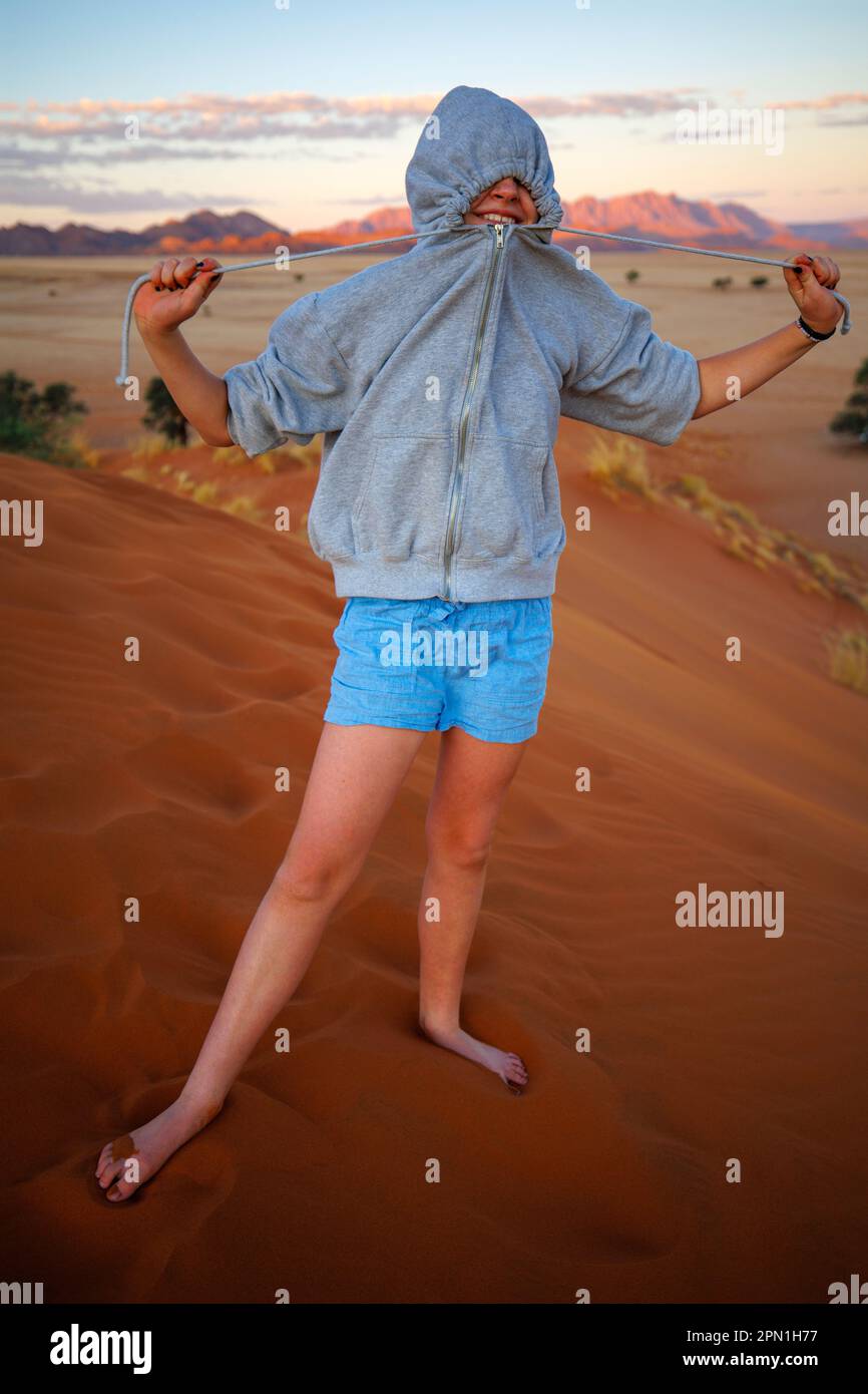 Girl covering her face with grey hoodie on sand dune Stock Photo