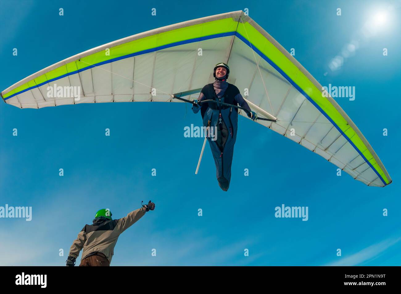 Aerial stunt. Hang glider pilot gives high five to his friend standing