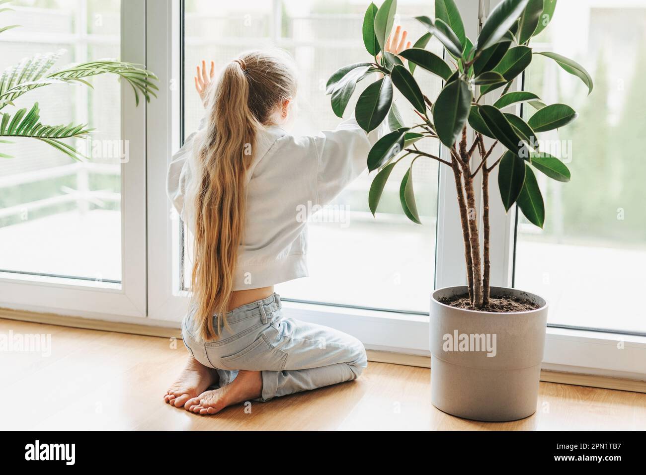 Lonely sad little girl sitting by the window. Stock Photo