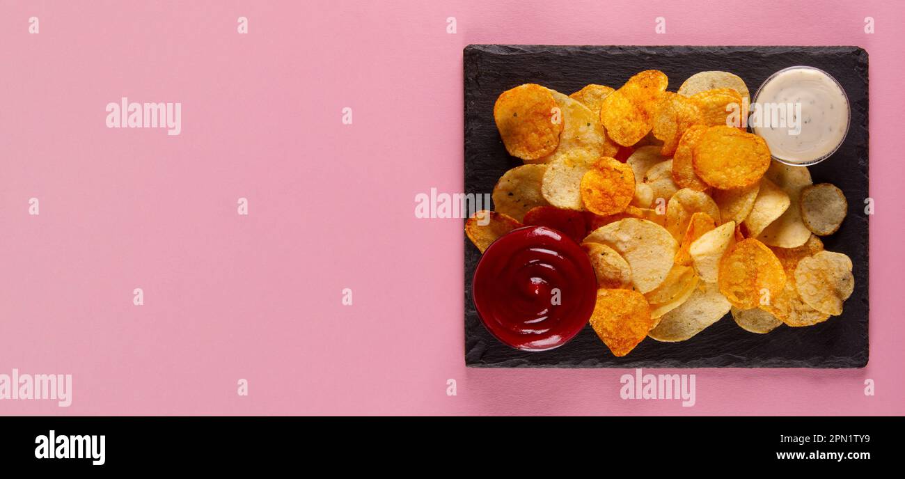 Perfectly salted and crispy potato chips with creamy white and savory red dip on pink background Stock Photo