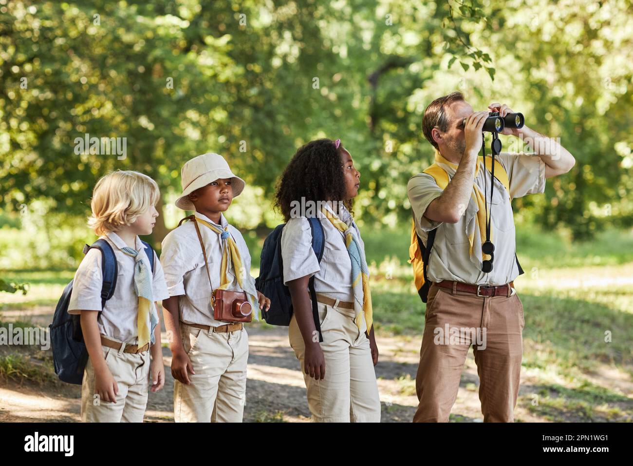 Group of scouts in forest exploring nature with adult scout leader