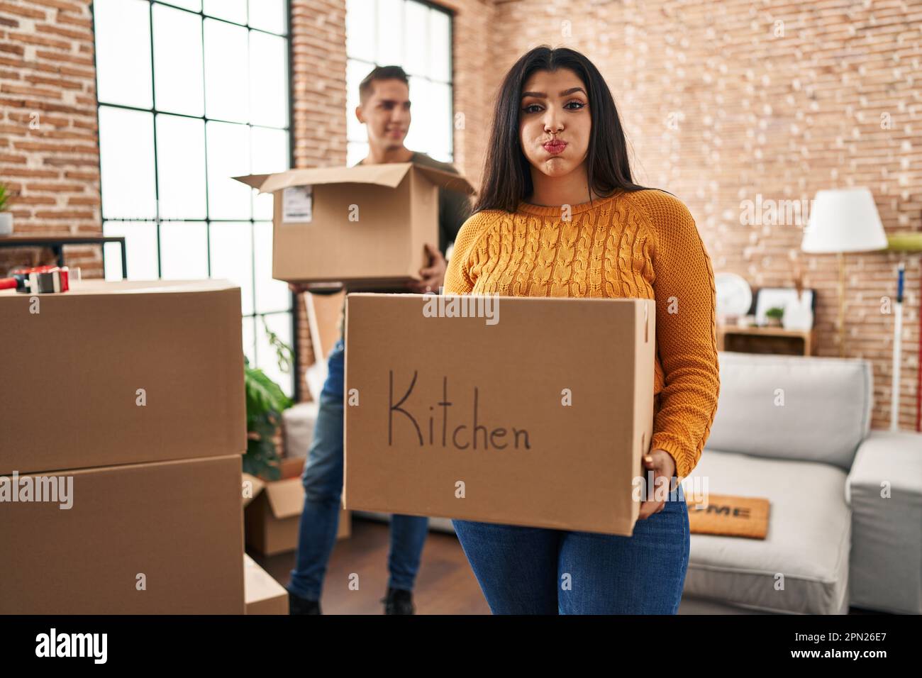 Young couple moving to a new home with cardboard boxes puffing cheeks ...
