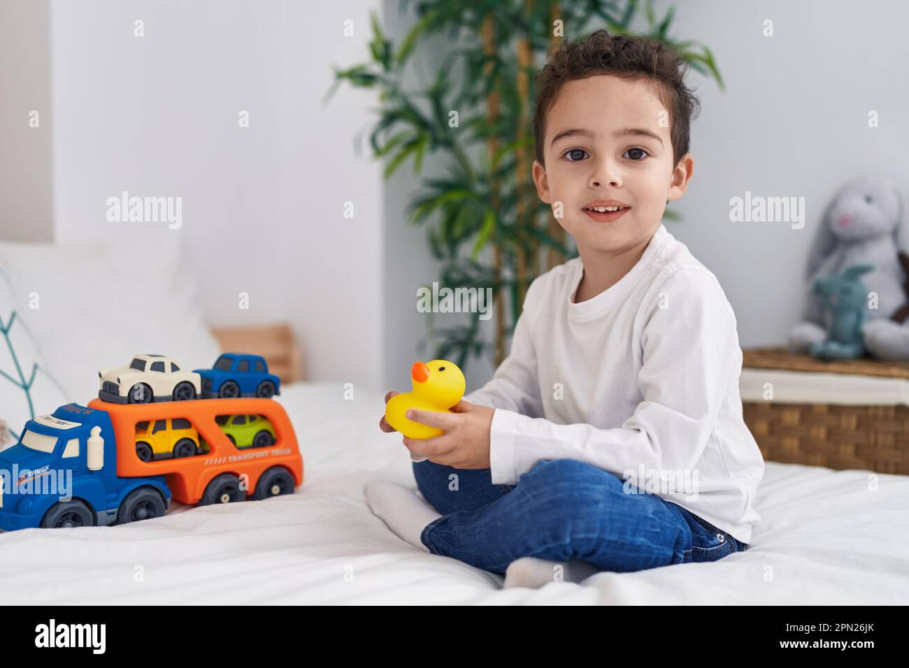 Adorable hispanic boy holding duck toy sitting on bed at bedroom Stock ...