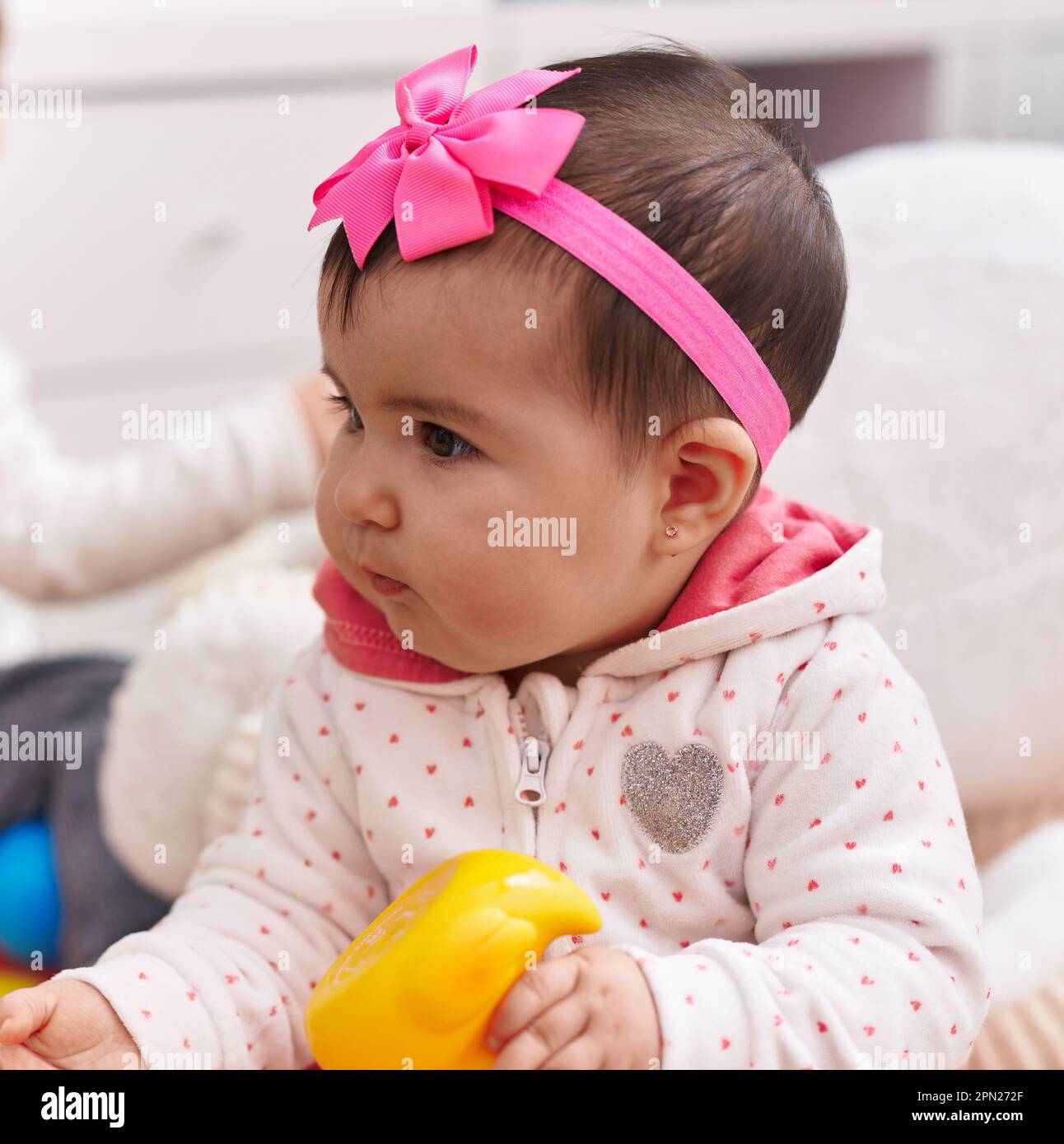 Adorable hispanic baby sitting on floor holding duck toy at home Stock Photo