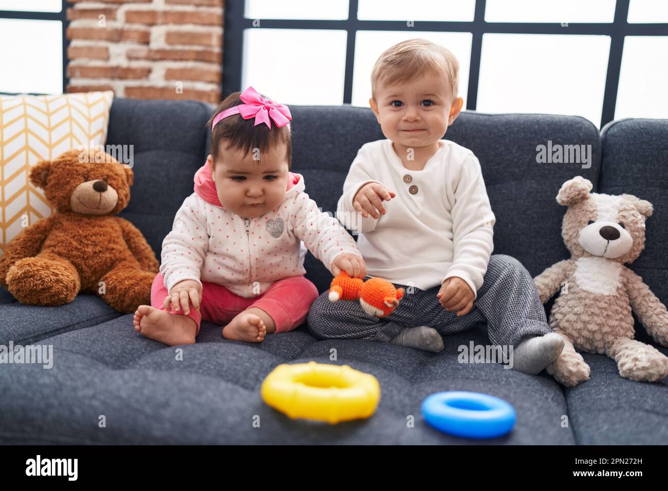 Adorable boy and girl playing with hoops game sitting on sofa at home ...