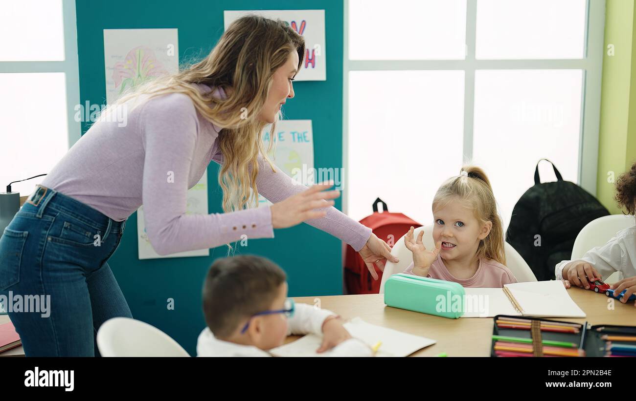 Woman with boy and girl having lesson sitting on table at classroom ...