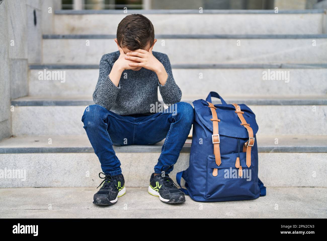 Blond Child Student With Worried Expression Sitting On Stairs At School 