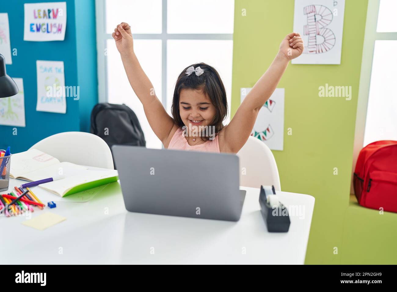 Adorable hispanic girl student using laptop with winner expression at ...