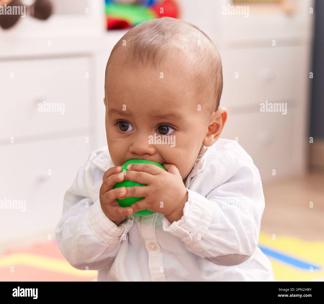 Adorable caucasian boy sucking ball sitting on floor at kindergarten Stock Photo - Alamy